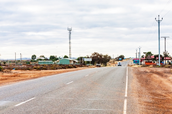 Two-lane road in a desert with brush and a couple small buildings